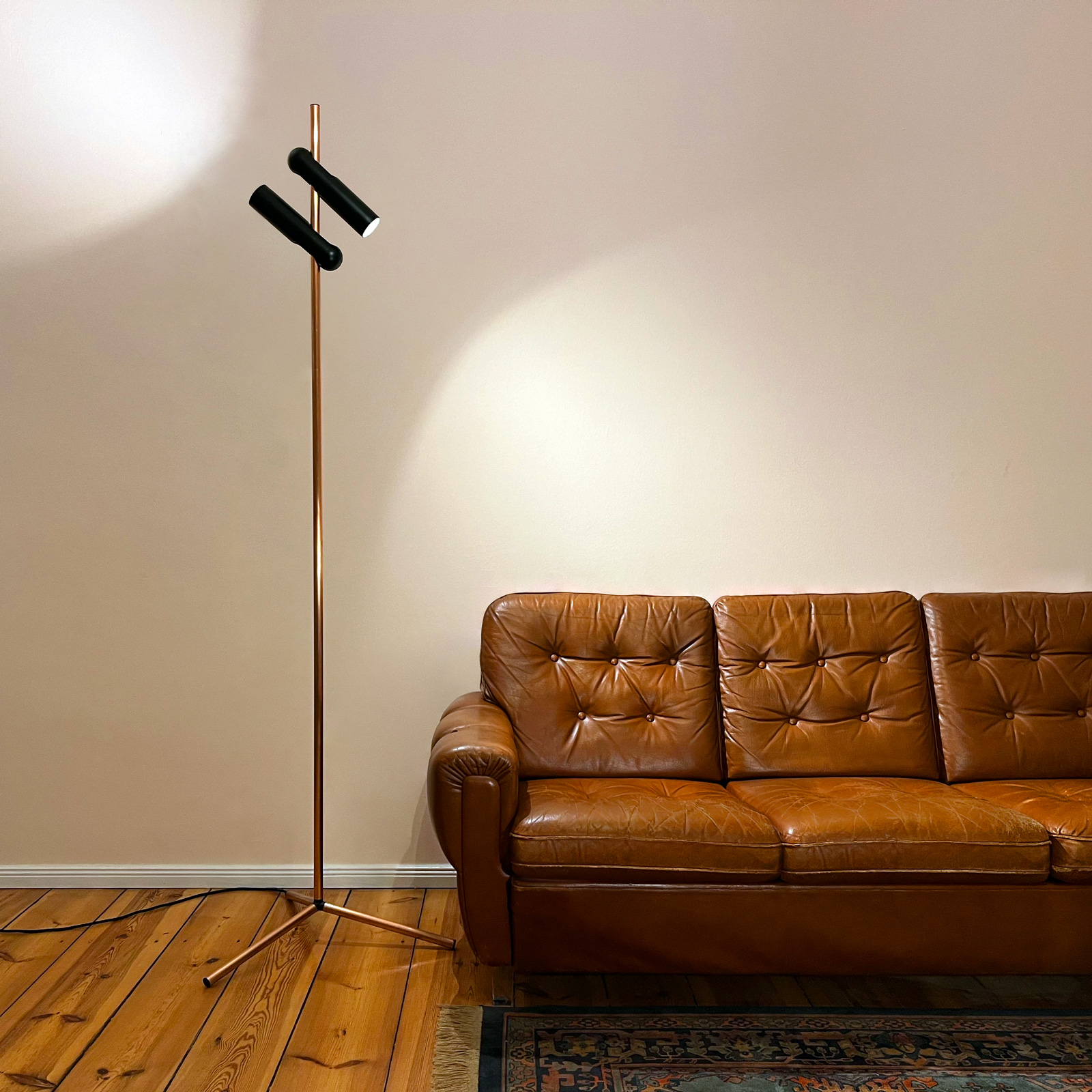 Photograph of the Tower light in a lounge room, next to a brown leather couch and colorful rug.